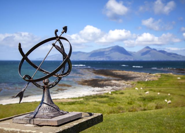 A circular ornament with an arrow in it, outdoors on the coast on the isle of Muck.