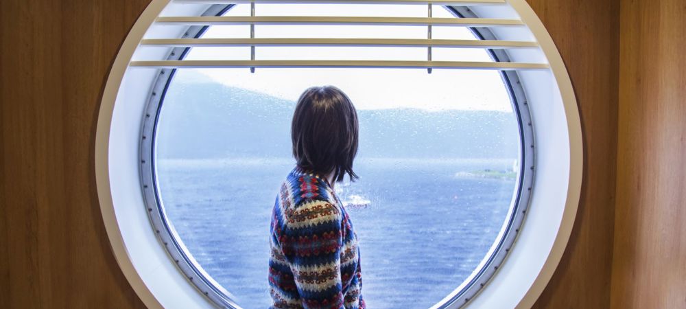 A passenger on the ferry sitting and looking out a round window