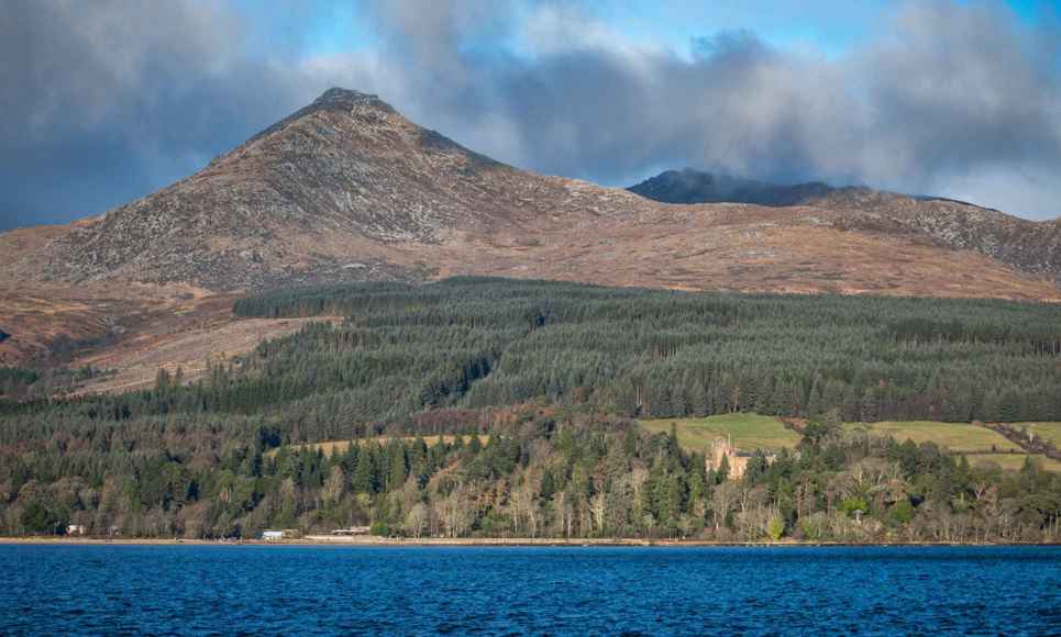 Goatfell, the highest peak on Arran, with woodland and water in the foreground.