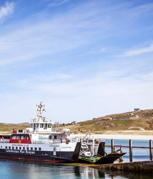 CalMac ferry MV Loch Alainn at Eriskay slipway on a bright day. Beach, a gentle hill and blue sky behind the ferry.