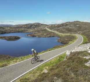 A cyclist riding on a single track road through the rocky Barra landscape.