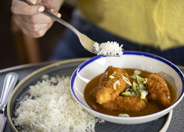 chicken katsu curry in a bowl sitting on a plate with a bed of white rice