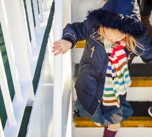 little girl walking down the stairs of the boat outside holding onto the handrail