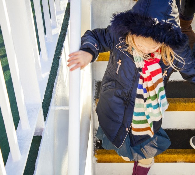 little girl walking down the stairs of the boat outside holding onto the handrail