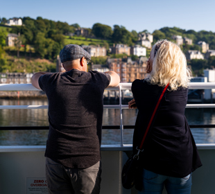 Two people standing looking over the ferry railings to the mainland