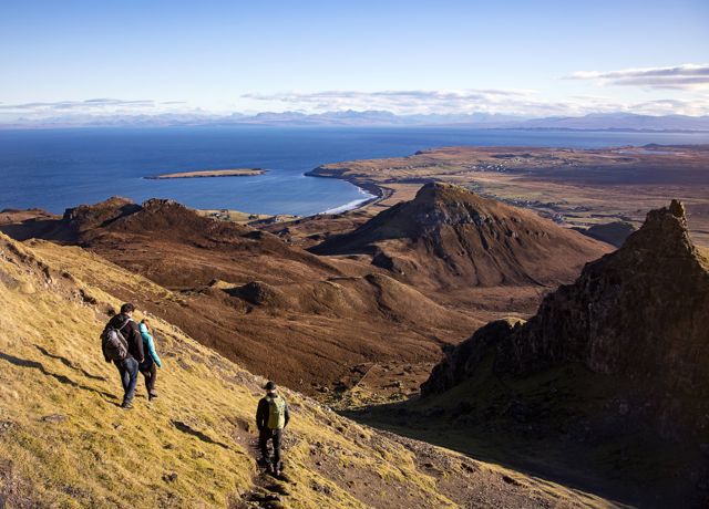 Hillwalkers descending a path. A stunning view of hill tops, coastline and across the water to the mainland.