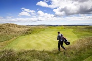 Man on golf course walking in the sun to green with his golf bag