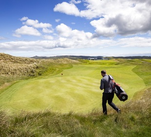 Man on golf course walking in the sun to green with his golf bag