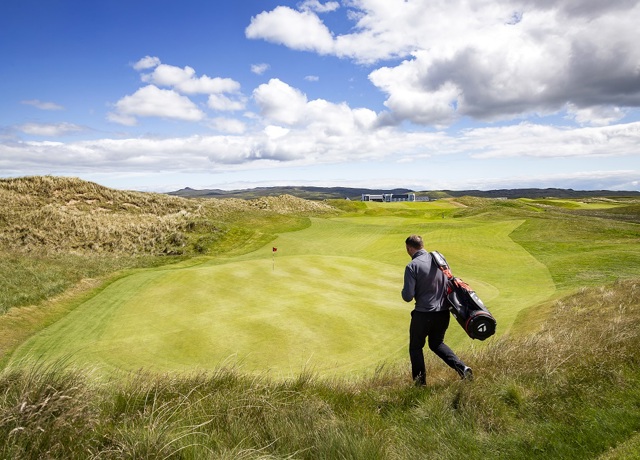 Man on golf course walking in the sun to green with his golf bag