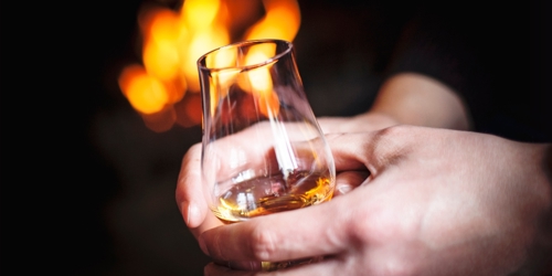 Hands holding a whisky glass witha fire in the background