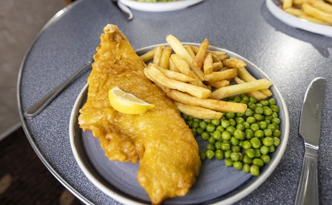 a plate of battered fish with a wedge of lemon on top with fries and peas. 