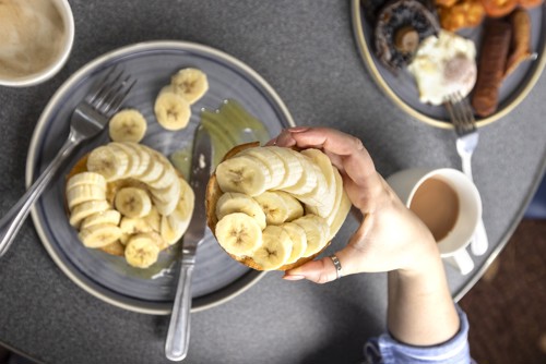 someone picking up a bagel with banana on top from a plate