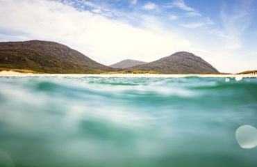 A view from in the water to a golden sandy beach with rolling hills in the background