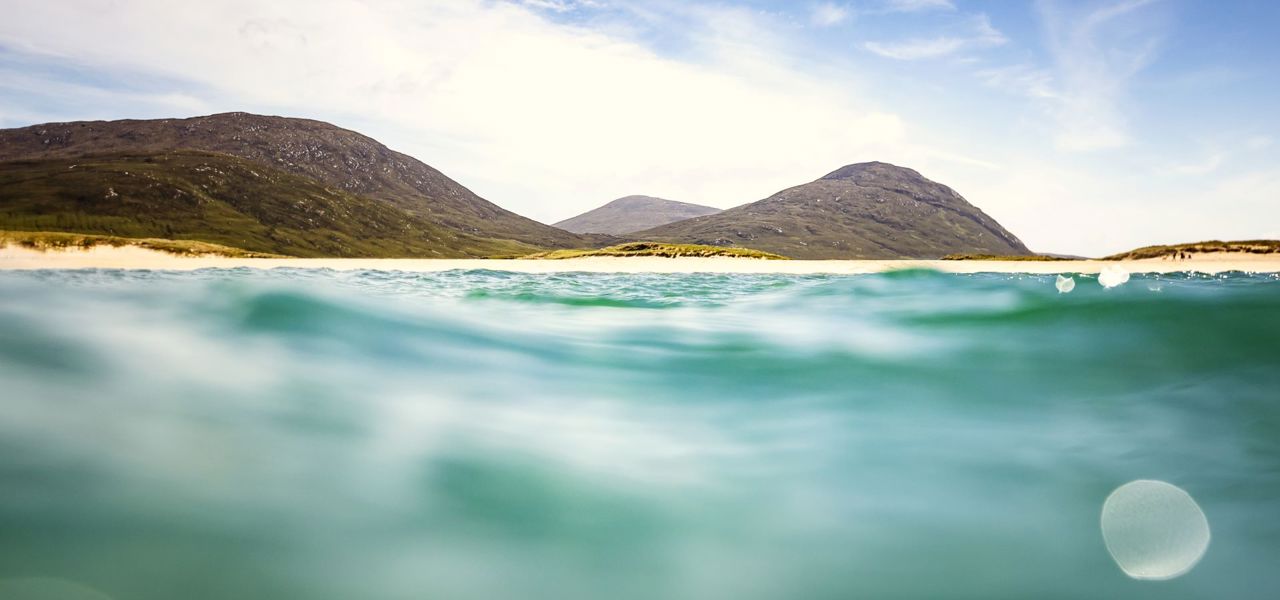 A view from in the water to a golden sandy beach with rolling hills in the background