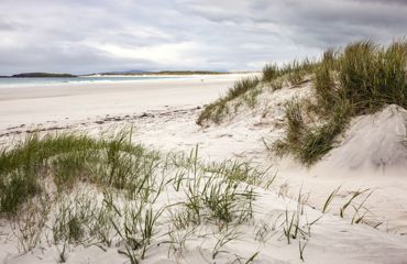 A deserted white sandy beach with sand dunes under a cloudy sky