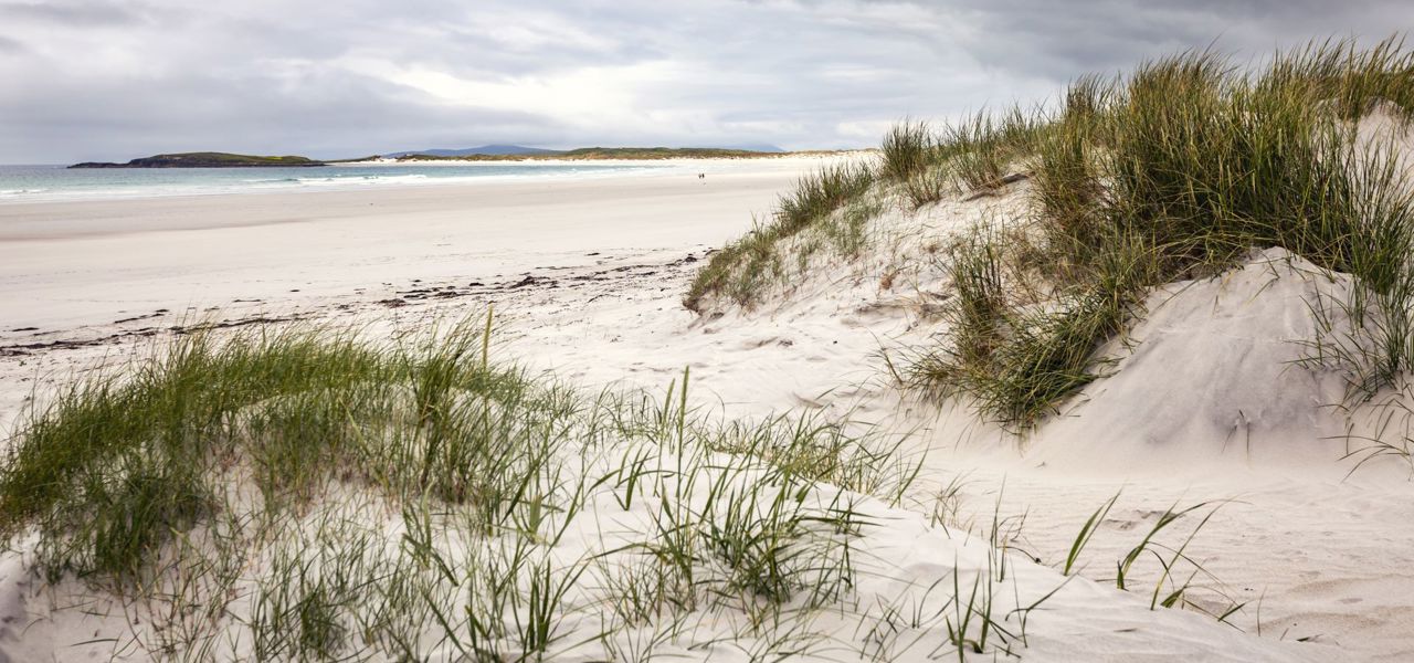 A deserted white sandy beach with sand dunes under a cloudy sky