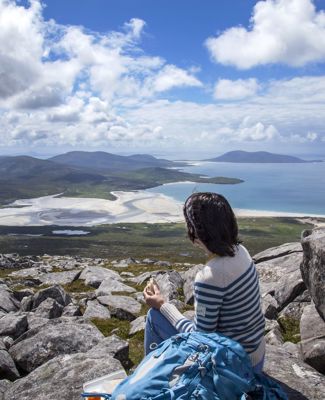 A hiker admiring the view down the rocky hillside to the golden sandy beaches and rolling hills in the distance