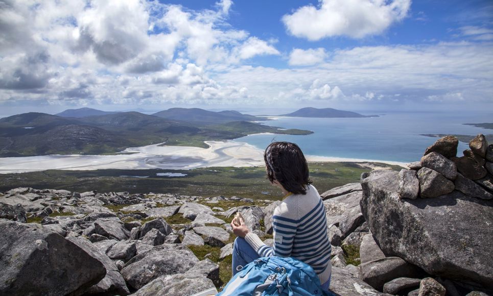 A hiker admiring the view down the rocky hillside to the golden sandy beaches and rolling hills in the distance