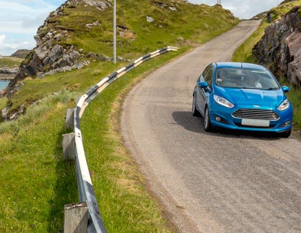 A blue car driving down a single track, coastal road