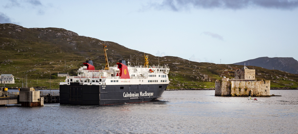 The Caledonian MacBrayne ferry to Barra sitting in the bay next to the rugged stone Kisimul Castle.