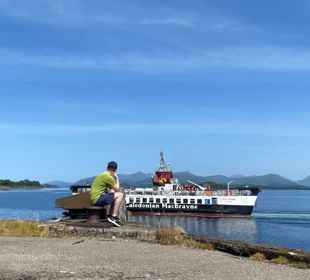 A Caledonian MacBrayne (CalMac) ferry sails to Lismore, with a person looking on from the harbour. Lismore.