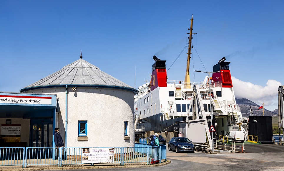 man standing outside Port Askaig port office with ferry to the right