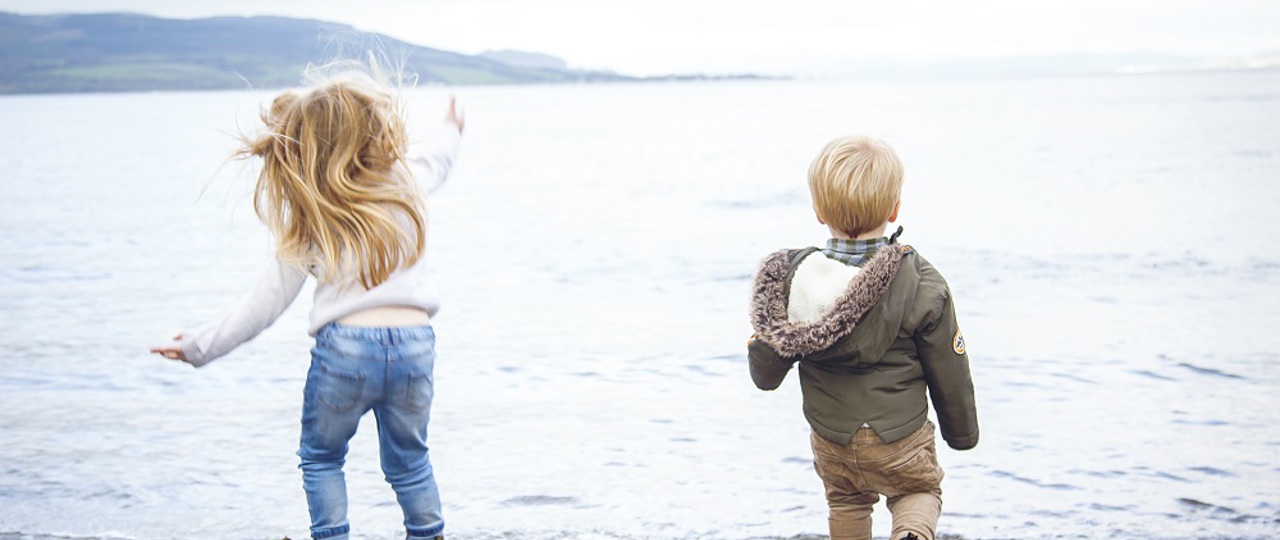 Two young kids on the beach throwing rocks into the sea