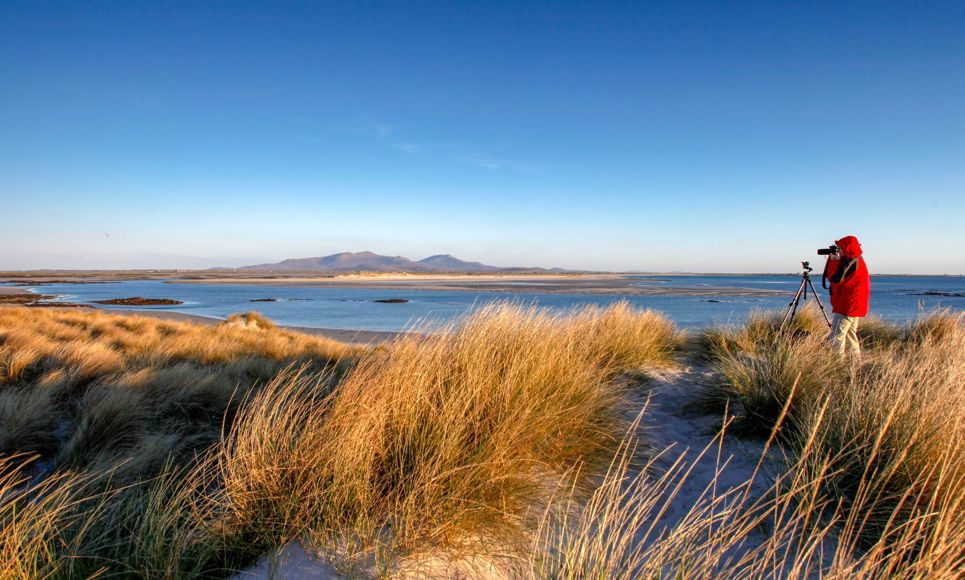 Wildlife photographer, standing in sand dunes at the beach at Liniclate Benbecula.