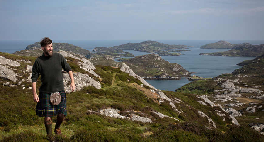 The Hebridean Baker wearing a kilt on top of a mountain with view out to sea behind him