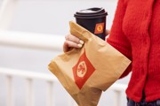 girl in a red sweater holding a brown paper bag with CalMac logo and a cup of coffee in  a black cup