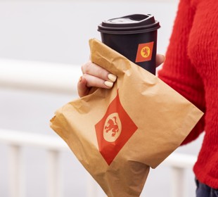 girl in a red sweater holding a brown paper bag with CalMac logo and a cup of coffee in  a black cup